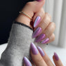 Lavender chrome almond press-on nails with iridescent shimmer finish — the trending purple nail design for 2026, paired with gold jewelry and cozy knit for a soft luxury look.