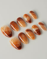 Onyx Shine press-on nails with warm amber marbling and polished gel surface