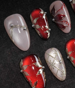 Carmine Court press on nails with sculpted gold leaves and silver pearls on deep red cat eye and a gold lattice on nude nails - image 1