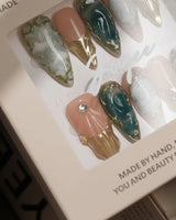 Close-up of Electric Muse press-on nails with green cat-eye marble, gold frames and sculpted 3D gel
