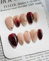 Gilded Rouge in extra short almond shape with warm burgundy gel and raised gold accents