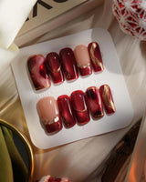 Molten Rouge press-on nails with deep red cat-eye shimmer, gold outlines and glossy crystal details