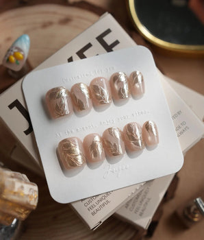 Plume press-on nails in extra short coffin shape — Elegant Nude, Brushed Gold Foil Feathers & Fluid Textures.