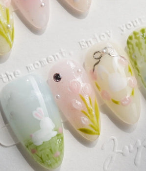Close-up of Easter garden press-on nails featuring delicate bunny illustrations, floral meadow scenes, and metallic silver bow details