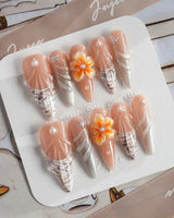Sunset Shore long stiletto nails with sunset coral, 3D blossoms, and shell accents