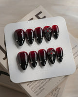 The Curse press-on nails in short stiletto shape — red to black gradient glossy chrome studs gothic cross charm