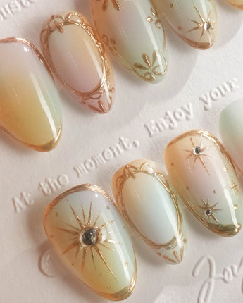Pastel Relic press-on nails with champagne gradient, gold linework, and soft starburst accents