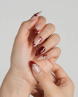 Crimson Petals press-on nails with nude base, deep red tips and delicate gold floral linework