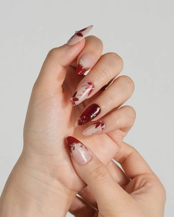 Crimson Petals press-on nails with nude base, deep red tips and delicate gold floral linework