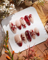 Crimson Petals press-on nails with glossy red French tips and gold outlined flower accents