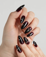 The Curse nail art close-up showing red to black gradient glossy chrome studs gothic cross charm details