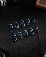 Absinthe press on nails in black with an emerald green cat eye halo and small silver star accents - image 3