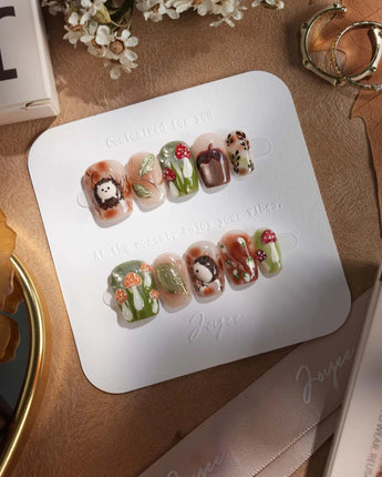 Autumn Tales press-on nails with warm forest colors, mushroom details and 3D hedgehog charm