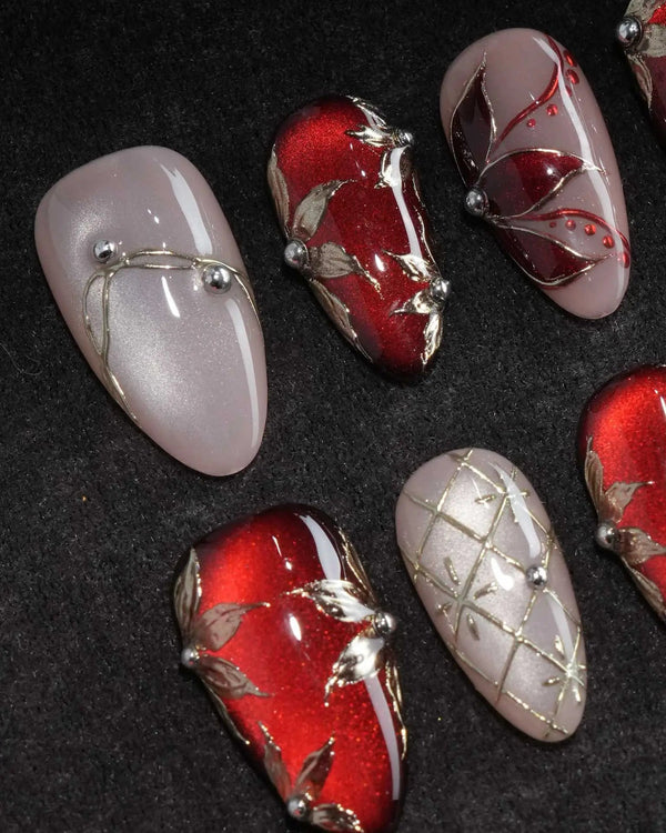 Carmine Court press on nails with sculpted gold leaves and silver pearls on deep red cat eye and a gold lattice on nude nails - image 1