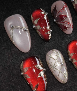 Carmine Court press on nails with sculpted gold leaves and silver pearls on deep red cat eye and a gold lattice on nude nails - image 1
