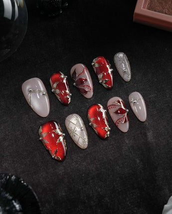 Carmine Court press on nails with sculpted gold leaves and silver pearls on deep red cat eye and a gold lattice on nude nails - image 3