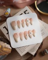 Ceramic press-on nails in short stiletto shape — Classic Nude Pink Ombré, 3D White Florals & Minimalist Rhinestones.