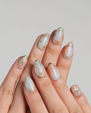 Pastel Relic nail set with milky champagne shimmer, delicate gold lines, and starburst details