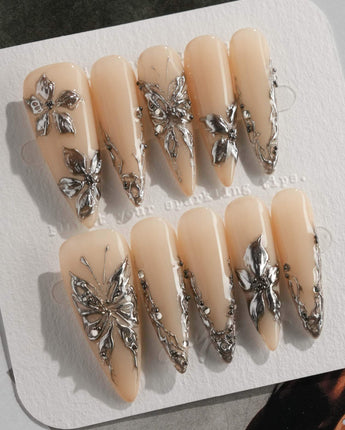 Chrome Rebellion press-on nails in long stiletto shape — Nude, 3D Silver Butterflies & Liquid Metal.
