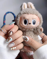 CocoaBoo Labubu close-up of brown chrome, plaid nail art, and playful collectible-inspired face