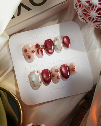 Coquette Red press-on nails with deep red cat-eye shine, gold trim and coquette bow styling