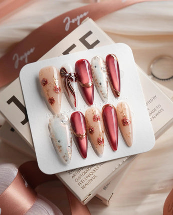 Coquette Red long stiletto press-on nails with deep red chrome, gold outlines, bows, and rose accents