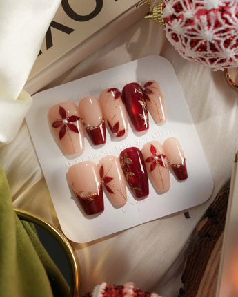 Crimson Petals press-on nails with nude base, red French tips and gold outline florals