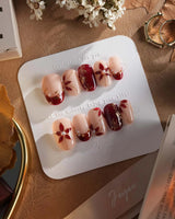 Crimson Petals press-on nails with deep crimson tips and delicate gold outlined flowers