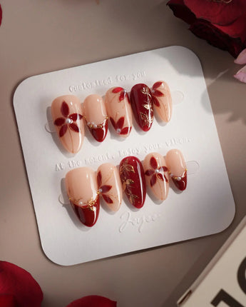 Crimson Petals press-on nails with glossy crimson French tips and delicate gold floral details