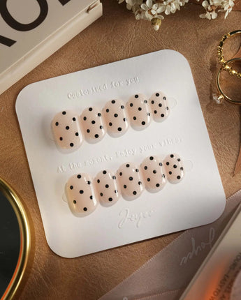 Dot Noir press-on nails with chic black polka dots on a nude glossy base