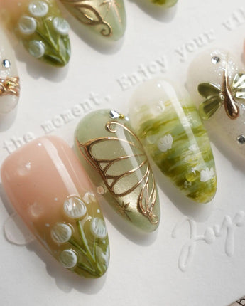 Dragonfly Pond press-on nails with 3D gold dragonfly and butterfly charms, hand-painted green lily pad pond scenes, and white lily of the valley on almond nails