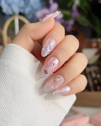 Dreamglow fairytale nails with soft pink shimmer, sculpted bows, and delicate pearls