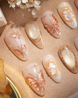 Close-up of Dreamland Glow press-on nails with sculpted gold butterflies and autumn bridal details