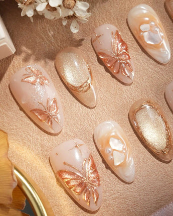 Close-up of Dreamland Glow press-on nails with sculpted gold butterflies and autumn bridal details