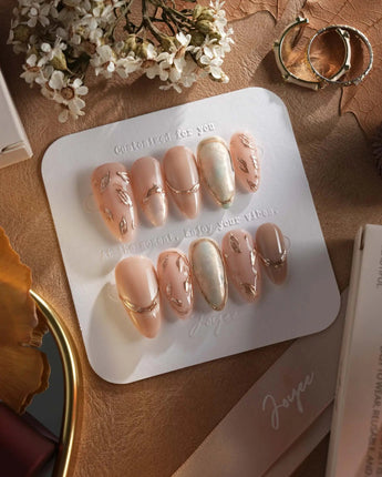 Earthy glow press-on nails with earthy nude peach color and gold foil leaf details