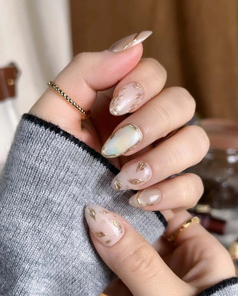 Earthy glow press-on nails with warm nude peach tones and gold foil leaf nail art