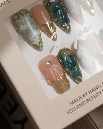 Close-up of Electric Muse press-on nails with green cat-eye marble, gold frames and sculpted 3D gel