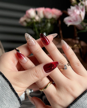 Close-up of Gilded Rouge nails with amber red gel and textured gold leaf accents
