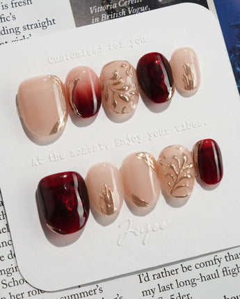 Gilded Rouge in extra short oval shape with amber red polish and gold leaf texture