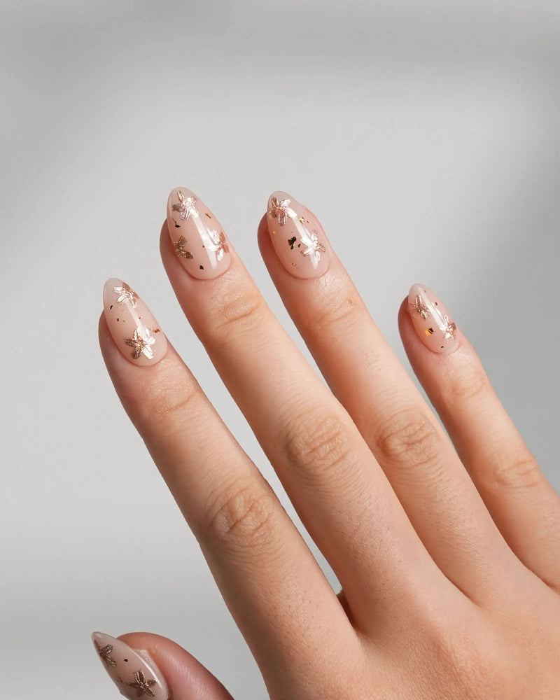 Glow Petals handmade press-on nails featuring gentle nude pink base with rose gold flower accents and gold flakes on extra short almond shape