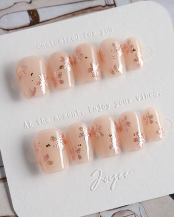 Glow Petals press-on nails in extra short coffin shape — Gentle Nude Pink, Rose Gold Flowers & Gold Flakes.