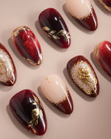 Close-up of Gilded Merlot press-on nails with deep red cat-eye, gold foil and rose relief details