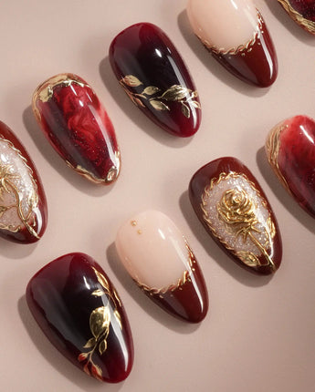 Close-up of Gilded Merlot press-on nails with deep red cat-eye, gold foil and rose relief details