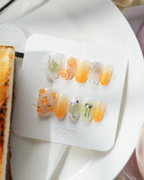Iced Punch short oval press-on nails with warm orange jelly gradient and fruit charms