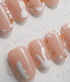 Meadow Bunny press-on nails with hand-painted white rabbits, gold foil flakes, and leaf details on short square nude nails