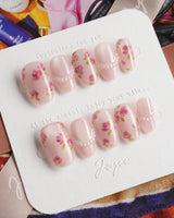 Meadow Glow short oval nails with soft pink base, red floral prints, and pearl chain accents