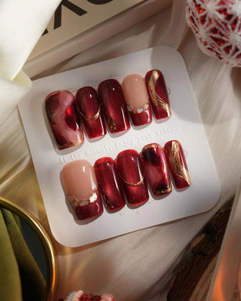 Molten Rouge press-on nails with deep red cat-eye shimmer, gold outlines and glossy crystal details