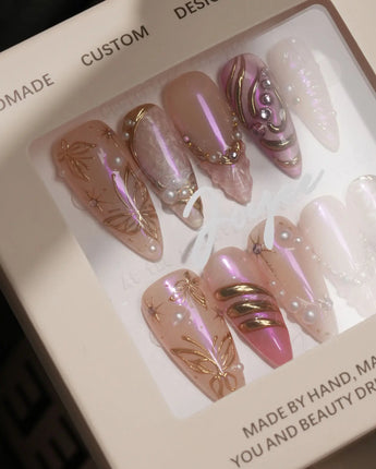 Close-up of Neon Kiss press-on nails with pink chrome butterfly wings, pearls and raised gold lines