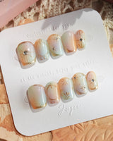 Pastel Relic press-ons with sheer milky shimmer, gold line details, and soft pastel glow