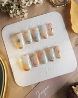 Pastel Relic press-on nails with pearly pastel base, gold linework, and polished gel shine